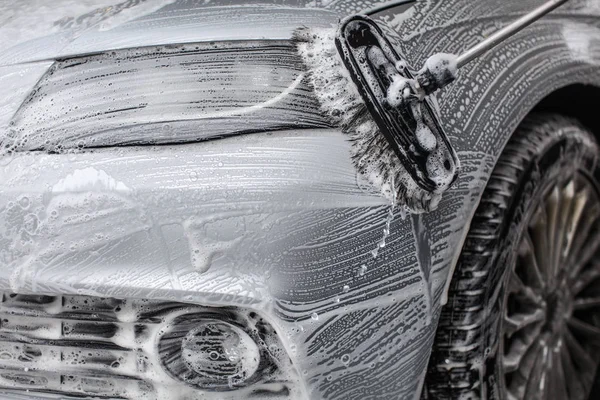 Detalle en la parte delantera del coche cubierto de espuma de jabón, lavado con cepillo en lavado de coches . —  Fotos de Stock