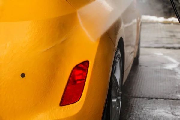 Detalle en la parte posterior del coche amarillo oscuro que se lava con estrea de agua de chorro — Foto de Stock