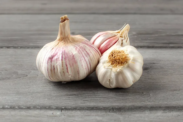 Garlic bulbs, purple cloves under cracked skin on gray wood tabl — Stock Photo, Image