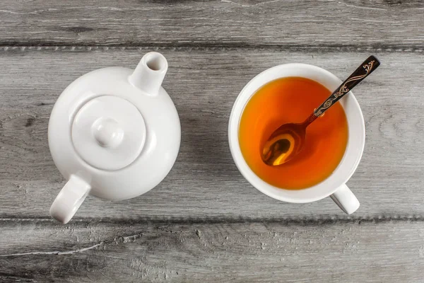 Table top view on small white teapot and cup full of hot amber t — Stock Photo, Image