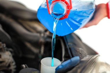 Woman pouring blue antifreeze liquid into dirty car. clipart