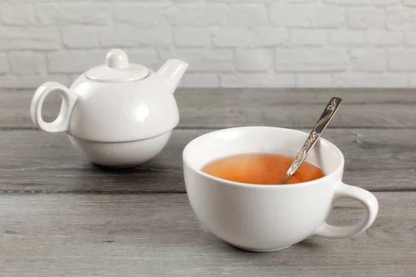 White ceramic teapot and cup of hot amber tea on gray wood desk. — Stock Photo, Image