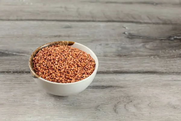 Piccola ciotola piena di grano saraceno posta sulla scrivania in legno grigio . — Foto Stock