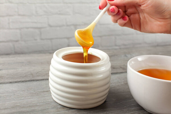 Detail on woman holding small ceramic  spoon, filled with honey,