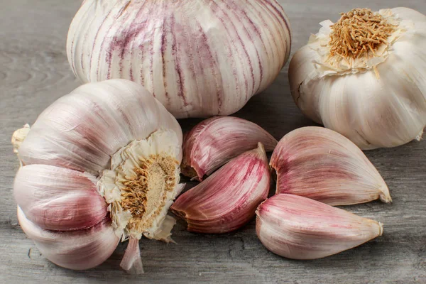 Detailed photo of garlic bulbs, and purple cloves on gray woode — Stock Photo, Image