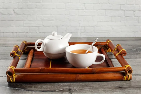 Small white ceramic teapot and cup of hot steaming black tea wit