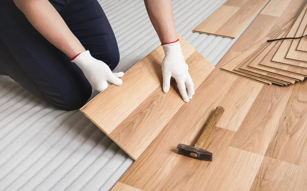 Man installing laminated floor, detail on wooden tile being fitted, over white foam base layer