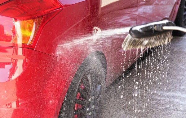 Rode auto gewassen in zelfbediening carwash, detail op wit zeepschuim spuiten van wasborstel, druppels druipend op natte grond — Stockfoto