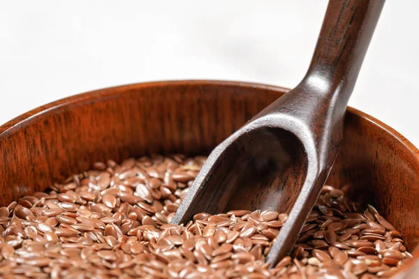 Common flax linseed - Linum usitatissimum - small wooden bowl, closeup on wooden spoon in heap of seeds — Stock Photo, Image