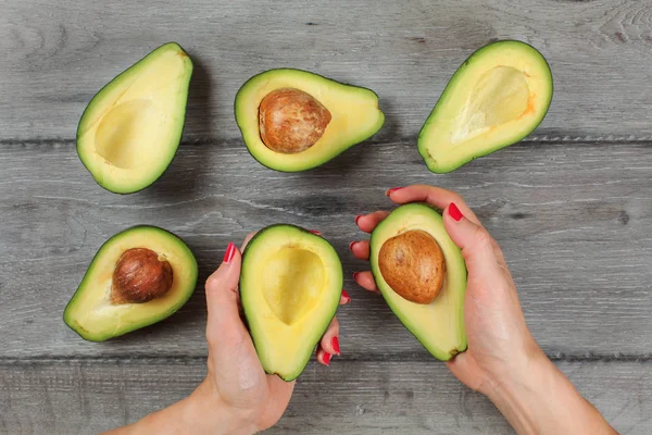 Tabletop view - woman hands with red nails, hold avocados cut in — Stock Photo, Image