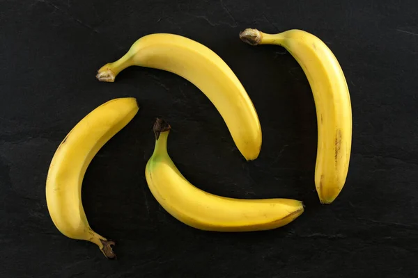 Flat lay foto - 4 bananas na mesa preta . — Fotografia de Stock
