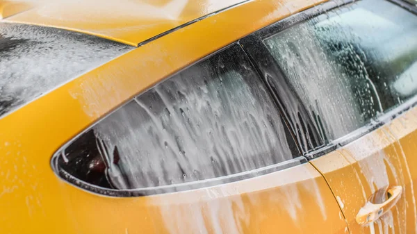 Coche amarillo lavado en auto servir lavado de coches, champú pulverización de h —  Fotos de Stock