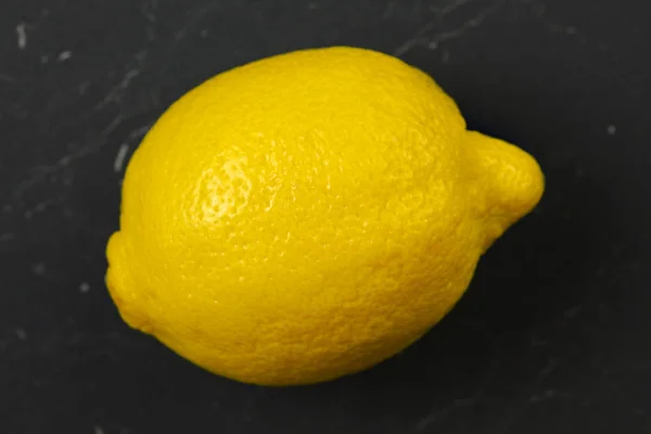 Single lemon on dark marble board.