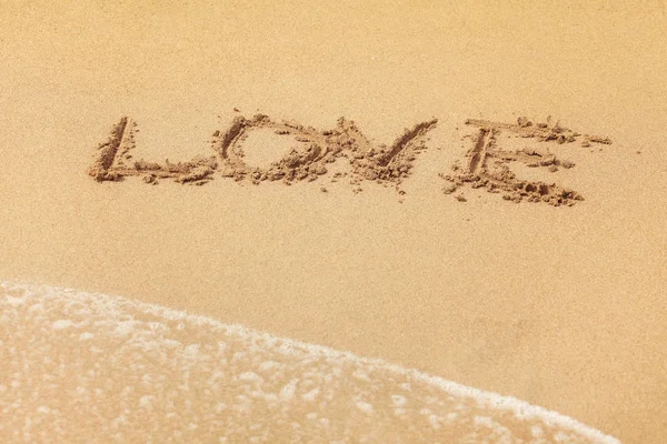 Palabra de AMOR escrita en arena mojada en la playa, el sol brilla sobre . — Foto de Stock