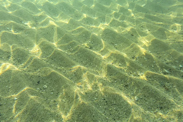 Underwater photo - seafloor, sun shines on sand "dunes" in shall