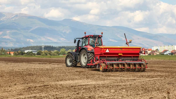Red tractor pulling sowing trailer behind over empty field. Some — Stock Photo, Image