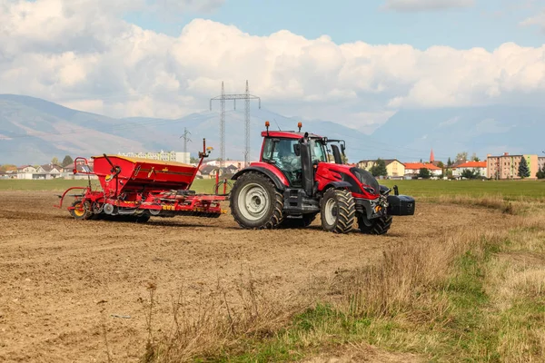 Tractor rojo sembrando, tirando del remolque de la sembradora detrás, en campo seco — Foto de Stock