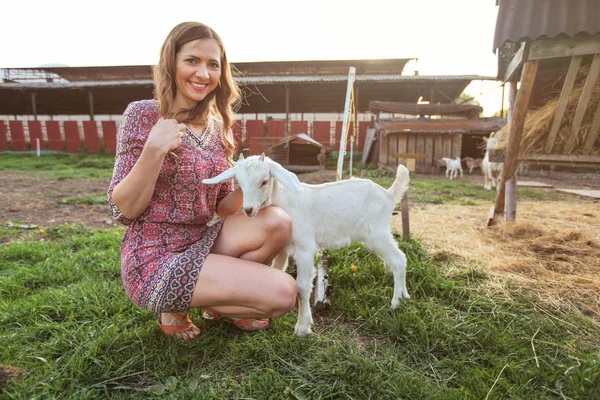 Mujer joven agachada, jugando con el cabrito de cabra, sonriendo, behi granja —  Fotos de Stock