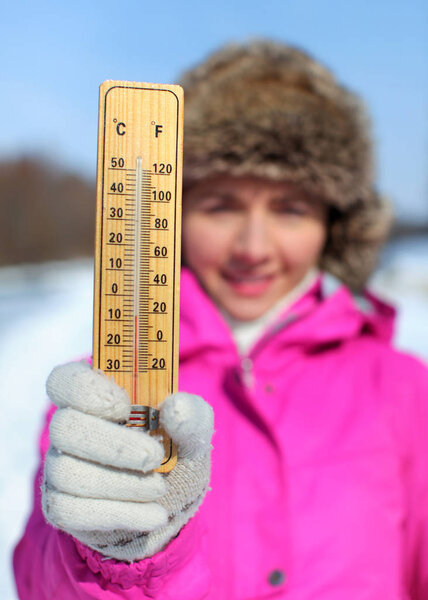 Young woman in pink jacket holds wooden thermometer outside on s