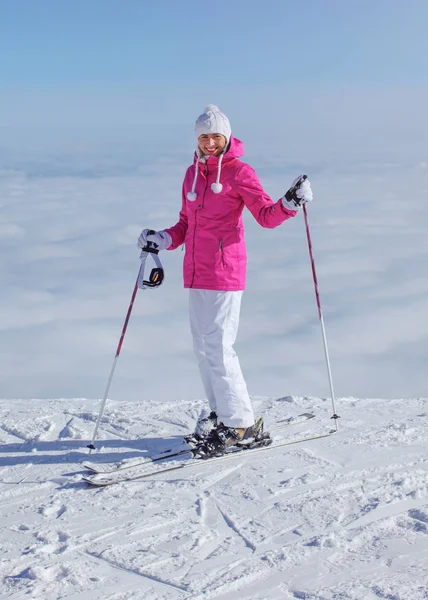 Woman in pink jacket, ski poles and skis, standing at the edge o