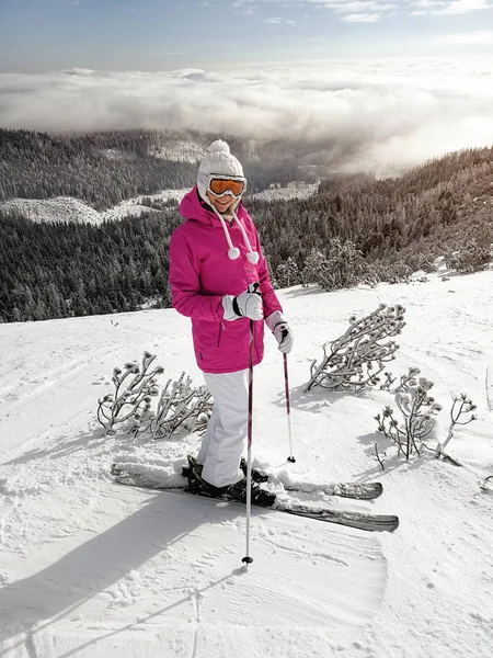 Девушка в розовой куртке, лыжах, лыжных палках, очках и шляпе, по — стоковое фото