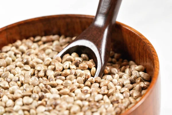 Soyulmamış kenevir - Kenevir sativası - küçük, koyu ahşap bir kâse içinde, kaşıkla, yakın plan detaylarıyla.