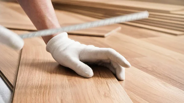 Instalación de piso laminado, detalle en las manos del hombre en guantes blancos, la celebración de cinta métrica sobre baldosas de madera — Foto de Stock