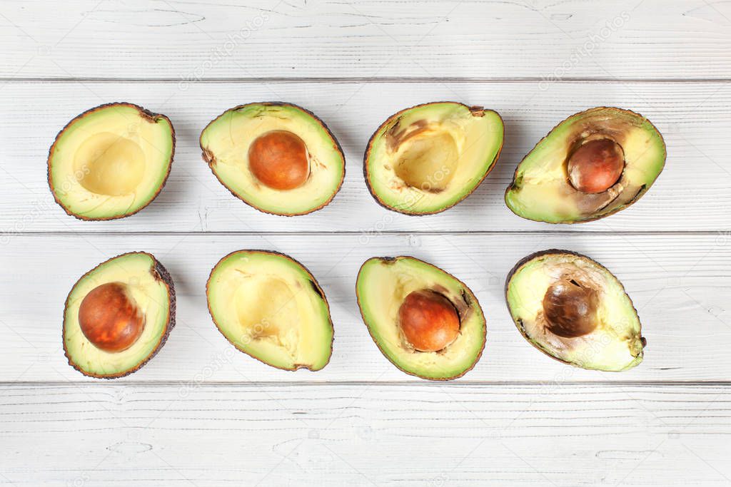 Avocado halves on white boards desk, view from above. Fruits arranged from unripe to overripe