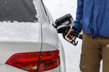 Man filling fuel to his diesel car at gas station in winter. Det