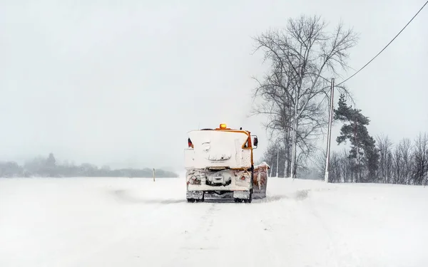 Camion de charrue orange sur route enneigée, ciel gris et arbres en ba — Photo