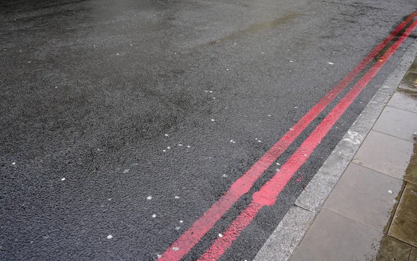 Doble línea roja cerca de bordillo en camino de asfalto húmedo. En Londres estos i — Foto de Stock