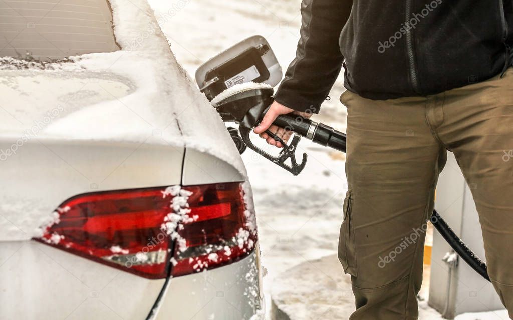 Man filling snow covered diesel car gas tank at the fuel pump, d