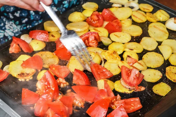 Patatas y tomates cortados en trozos pequeños a la parrilla en la parrilla eléctrica, mano borrosa sosteniendo tenedor de acero moviendo piezas humeantes sobre la superficie caliente — Foto de Stock