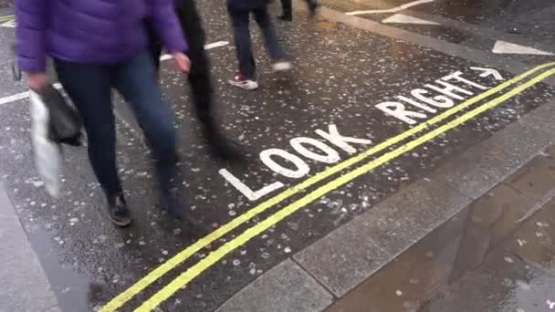 London, United Kingdom - February 01, 2019: Pedestrians crossing road, "Look right" text on wet asphalt, detail on their legs only — ストック動画