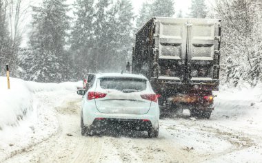 Orman yolunda trafik sıkışık, arabalar ve kamyonlar yavaş ilerliyor - yoğun kar fırtınası sırasında dağ geçidi