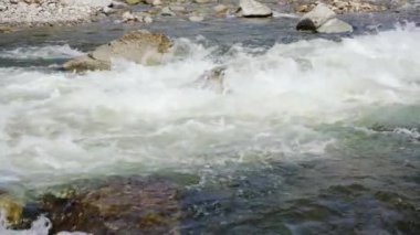 Beyaz su dalgaları baharda akan nehirde, taşlar ve kayalar görünür, yavaş çekim videosu
