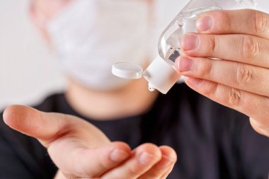 Arka planda ağız maskesi ve bulanık yüzü temizlemek üzere olan antibakteriyel jel tutan genç adamın detayları. Coronavirus ya da covid19 salgını önleme illüstrasyonu olarak kullanılabilir