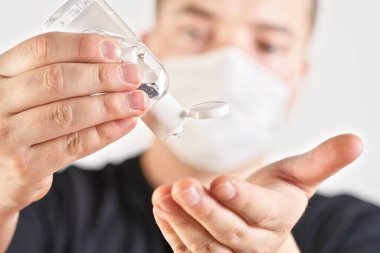 Arka planda ağız maskesi ve bulanık yüzü temizlemek üzere olan antibakteriyel jel tutan genç adamın detayları. Coronavirus ya da covid-19 salgını önleme illüstrasyonu olarak kullanılabilir