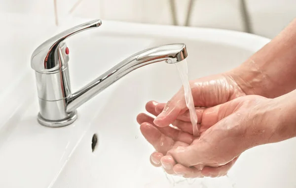 Young man washes his hands with soap under tap water faucet, closeup detail. Can be used as hygiene illustration concept during ncov coronavirus / covid 19 outbreak prevention