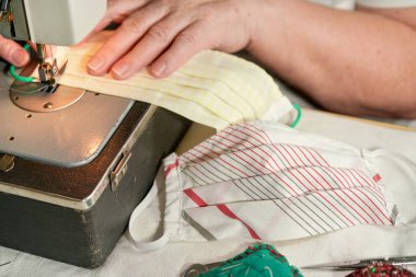 Yaşlı yaşlı bir kadın eski dikiş makinesinde çalışıyor. Coronavirus 'a karşı yüz maskesi yapıyor. Yayılıyor, maske kapanıyor.