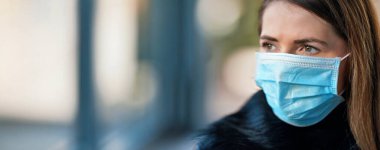 Tek kullanımlık mavi virüs kullanan genç bir kadın ağız maskesi takıyor, yakın plan bir portre - sol tarafta yazı için geniş bir afiş var. Coronavirus covid-19 salgın önleme kavramı