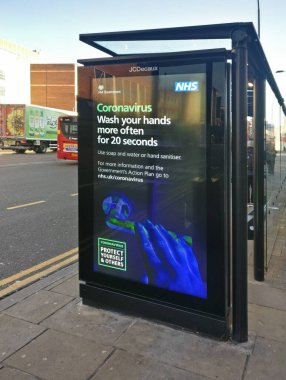 Londra, Birleşik Krallık - 31 Mart 2020: Londra Lewisham, Londra 'da otobüs durağındaki Coronavirus salgını sırasında el yıkama, kirli kapı koluna dokunan el resmi, NHS danışmanlık posteri