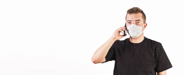 家を着ている若い男は 携帯電話で話している綿の顔の口の鼻ウイルスマスクを作った 白い背景 テキスト用の広いバナースペース コロナウイルスCovid 19発生中に使用することができます — ストック写真