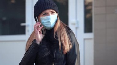 Koyu renk bereli ve tek kullanımlık mavi virüslü genç bir kadın cep telefonuyla konuşan ağız maskesi takıyor. Coronavirus covid-19 salgını önleme sırasında kullanılabilir