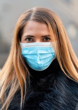Tek kullanımlık mavi virüs kullanan genç bir kadın ağız maskesi takıyor, yakın plan bir portre. Coronavirus covid-19 salgın önleme kavramı