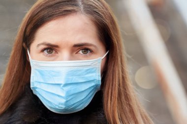 Tek kullanımlık mavi virüs kullanan genç bir kadın ağız maskesi takıyor, yakın plan bir portre. Coronavirus covid-19 salgın önleme kavramı