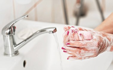 Genç bir kadın ellerini musluğun altında sabunla yıkıyor. Parmaklarda ayrıntı, mor ojeli tırnaklar. Kişisel hijyen kavramı - koronavirüs covid-19 salgını önleme