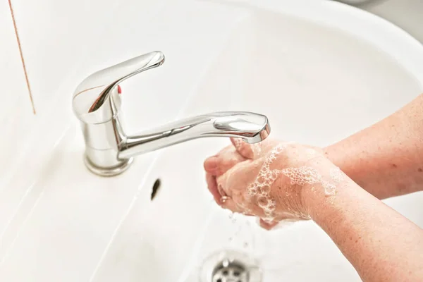 Senior elderly woman wash hands under tap water faucet. Can be used as hygiene illustration concept during coronavirus / covid-19 outbreak prevention