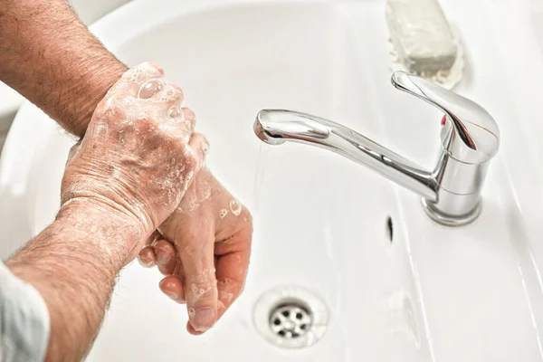 Senior elderly man his hands with soap under tap water faucet, detail photo. Hygiene illustration concept during ncov coronavirus / covid-19 outbreak prevention
