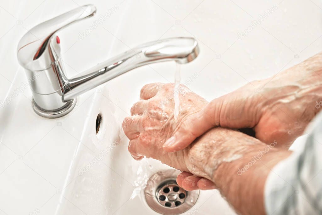 Senior elderly man his hands and wrist with soap under tap water faucet, detail photo. Can be used as hygiene illustration concept during ncov coronavirus / covid-19 outbreak prevention